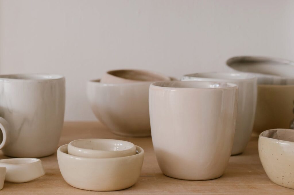 A collection of handcrafted ceramic bowls and cups in a minimalist style on a wooden table.