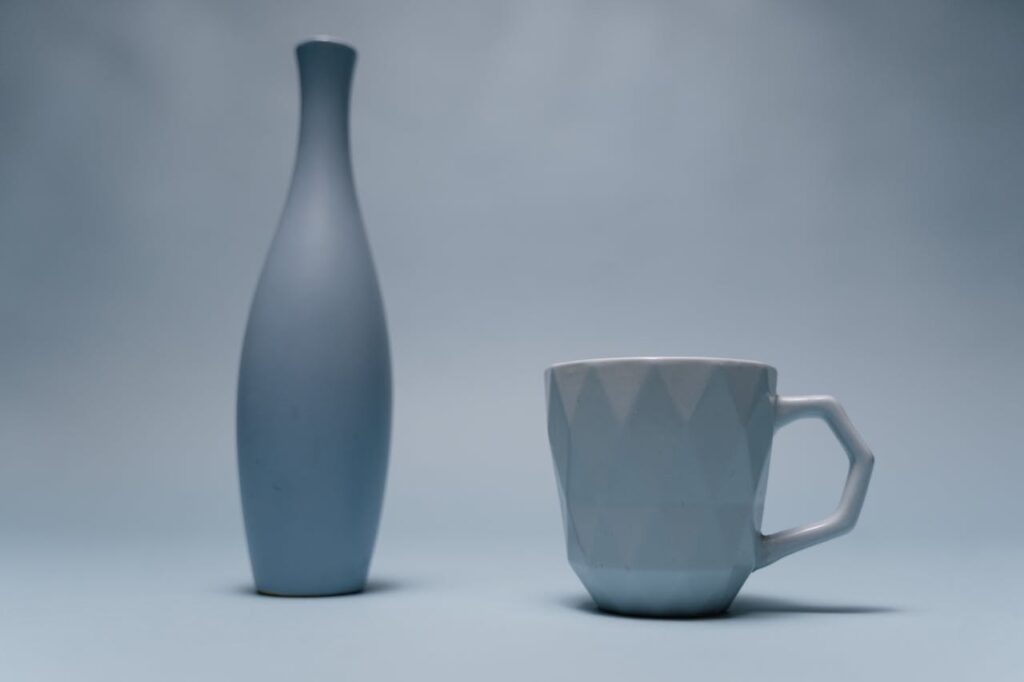 Elegant minimalist composition of a ceramic vase and cup on a soft blue background.