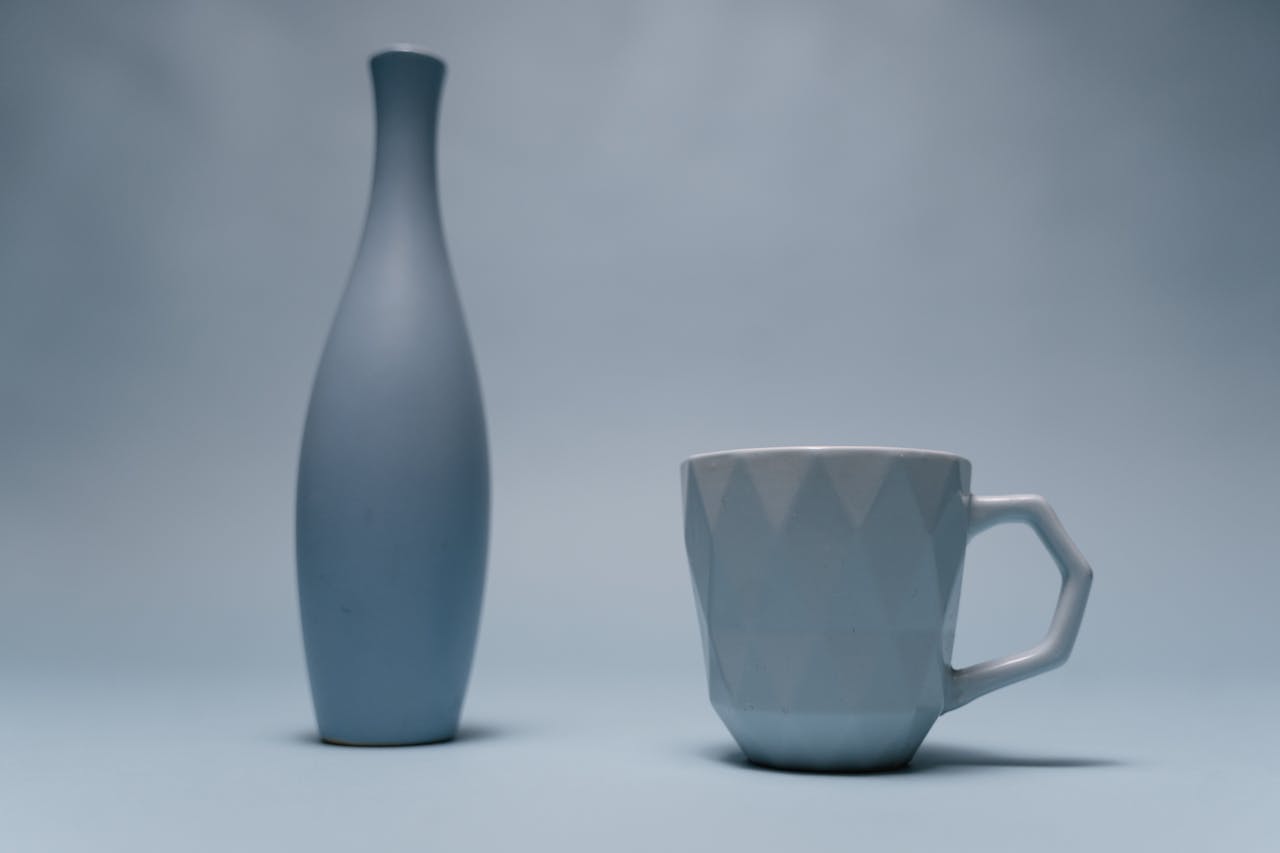 Elegant minimalist composition of a ceramic vase and cup on a soft blue background.